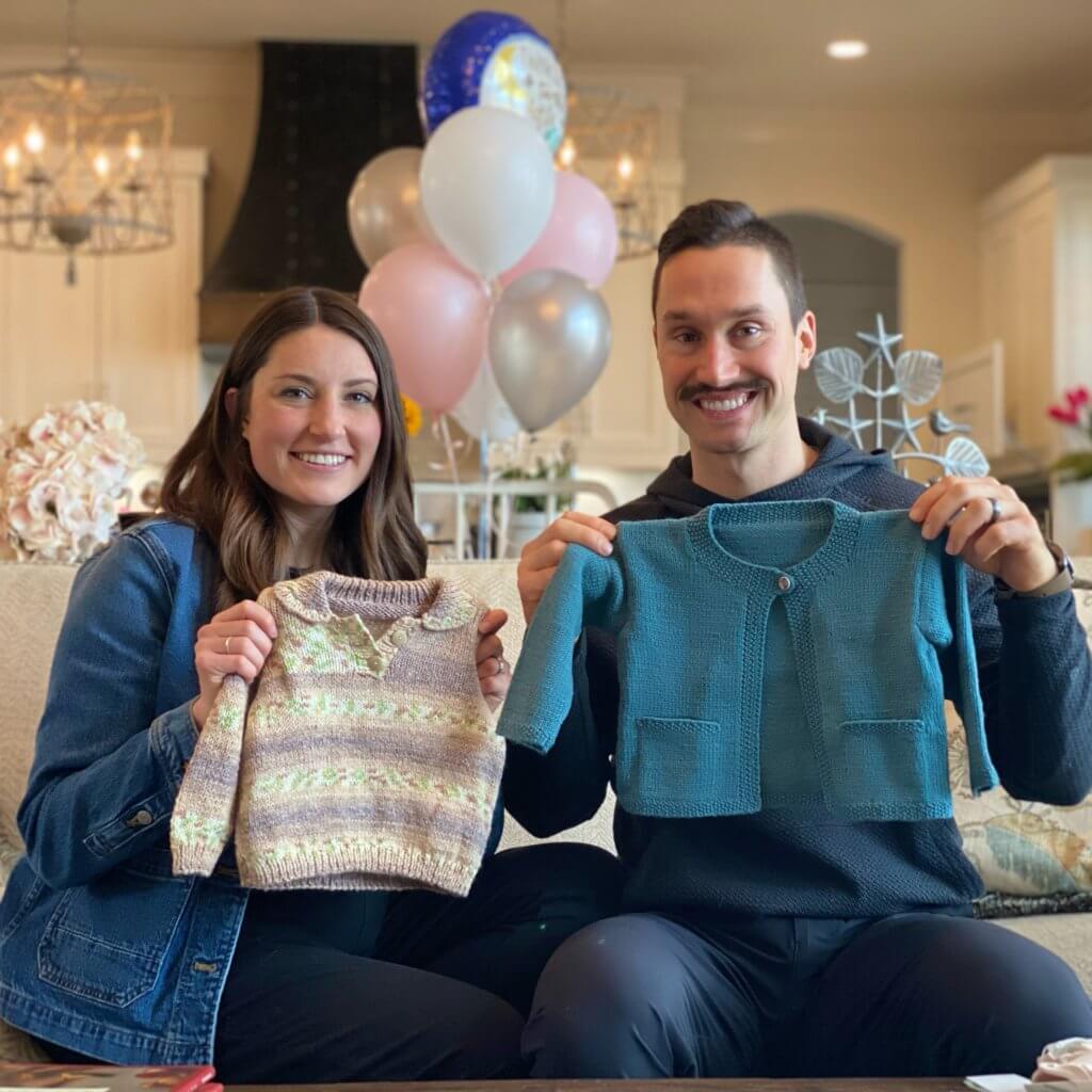 Nicole and Zach holding 2 handmade sweaters | hosting a virtual baby shower | Positively Jane 