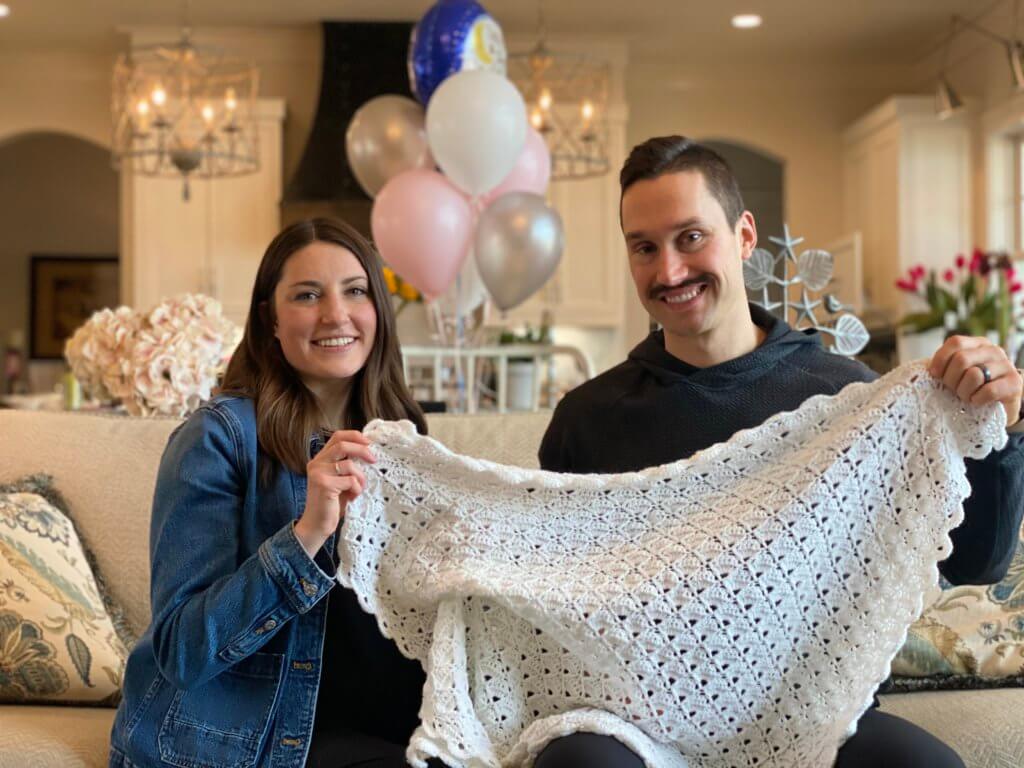 Nicole and 
Zach holding up a blanket they received from Grandma | hosting a virtual baby shower | Positively Jane 