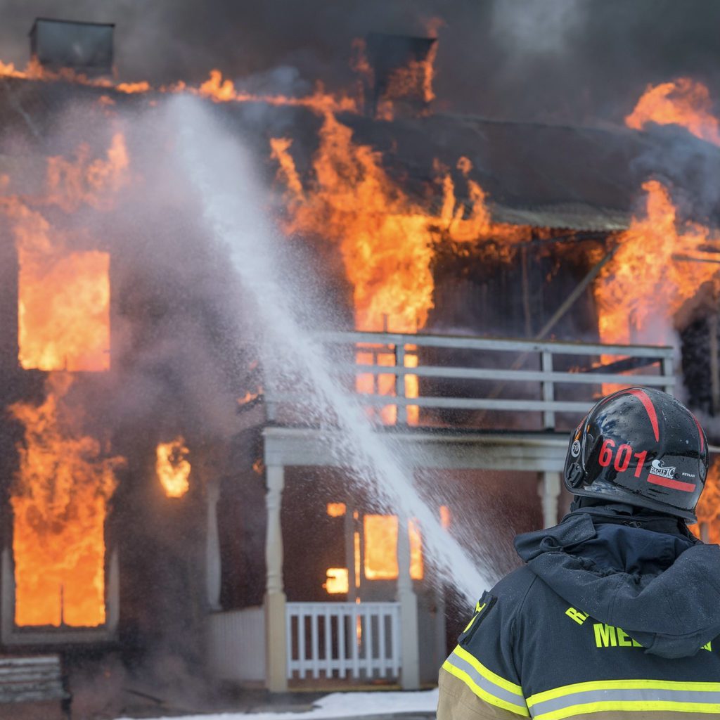 a home consumed with flames with a fire fighter trying to put it out | how big should your emergency fund be | what is an emergency fund | Positively Jane