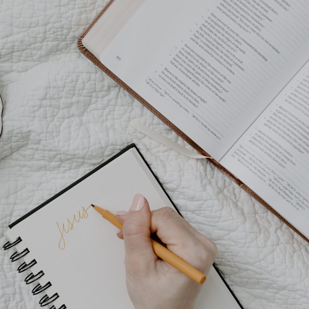 Person writing Jesus in a journal with her Bible Open | why I put my faith in Jesus | Positively Jane