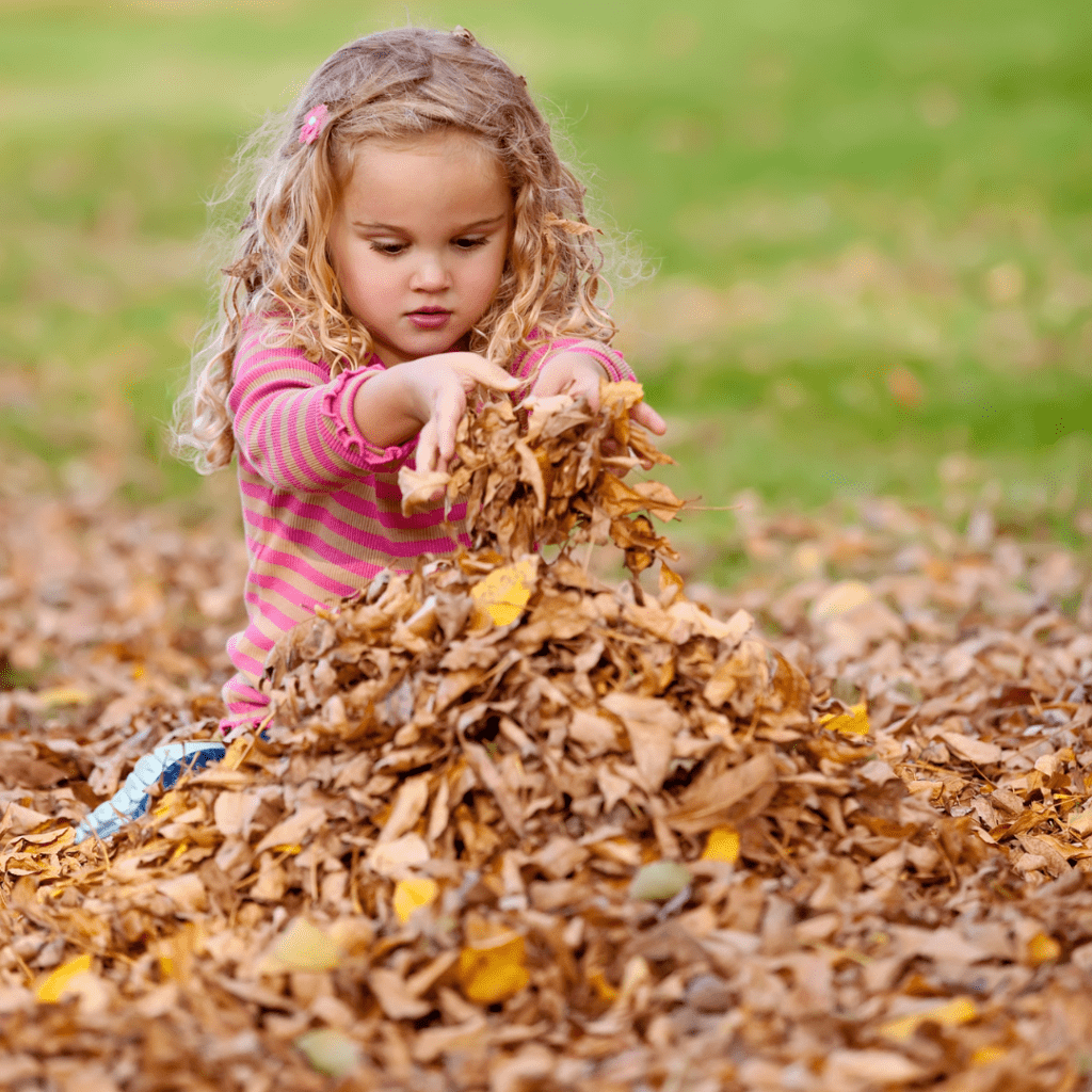 6 year old girl with long blonde curly hair sitting in pile of leaves | autumn the falling leaves |positively jane