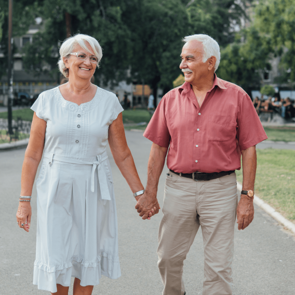 older couple, both with gray hair, walking down the street holding hands